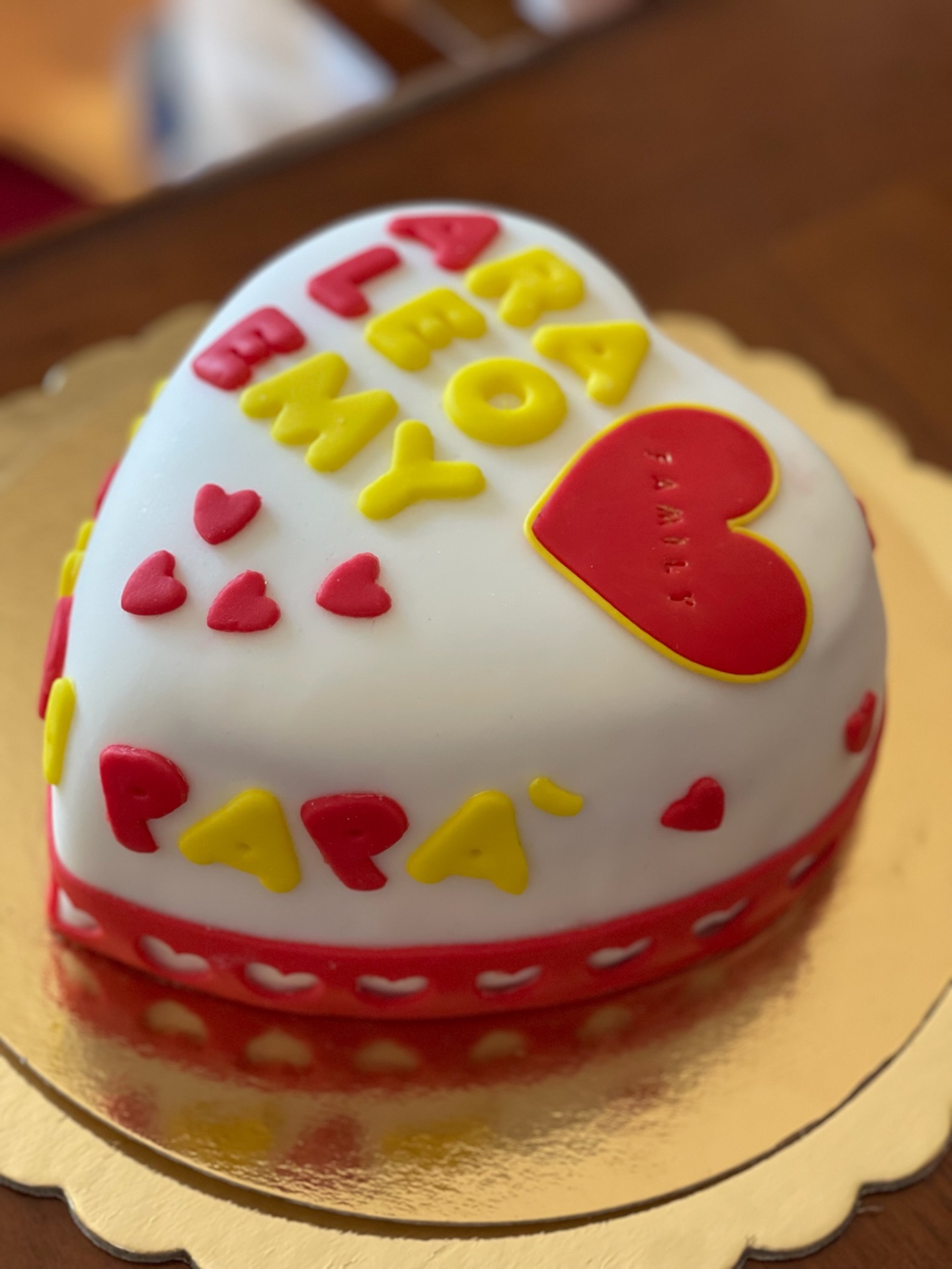 Torta a cuore bianca con lettere rosse e gialle e cuore family